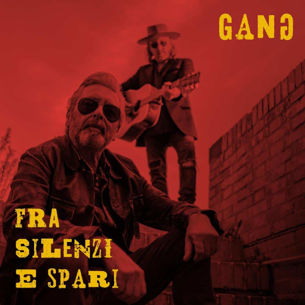 Copertina dell’album “Fra silenzi e spari” dei Gang. C’è una foto virata in rosso con i due componenti della band, il primo accucciato a terra in primo piano, il secondo in piedi con la chitarra dietro il primo, di fianco a un muretto. In alto a sinistra c’è il nome del gruppo, “Gang”; in basso a sinistra il titolo dell’album, "Fra silenzi e spari”.