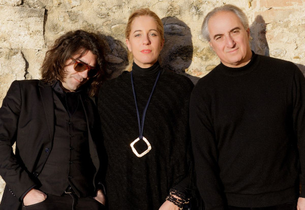 Una foto in formato panoramico che ritrae al centro, in piedi, Ginevra Di Marco, e al suo fianco a sinistra Francesco Magnelli, a destra Andrea Salvadori. Tutti e tre sono appoggiati a un muro di pietre e calce color beige e vestiti di nero.