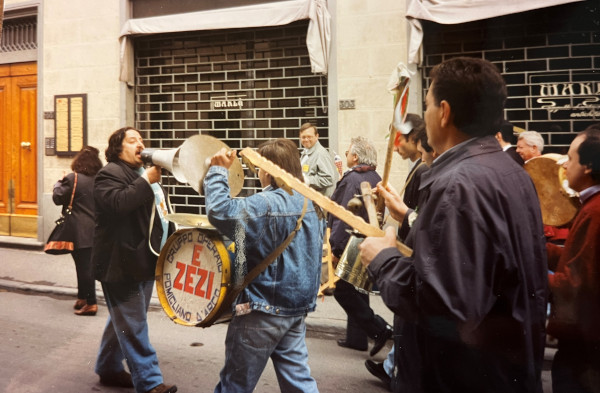 Una foto che ritrae Marcello Colasurdo con un grosso megafono in testa a un piccolo corteo di suonatori festanti in una strada di Sesto Fiorentino.
