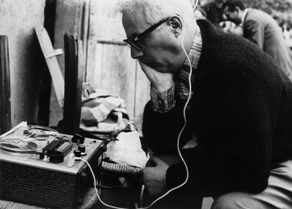 Una foto in bianco e nero di Clara Longhini che ritrae Gianni Bosio al “Maggio” di Costabona, nel 1967, di profilo, seduto su una sedia, all'aperto, davanti a un edificio (sembrerebbe una casa contadina), mentre riascolta una registrazione che ha effettuato poco prima tramite un auricolare nell’orecchio sinistro, collegato da un lungo cavo bianco a un grosso magnetofono a bobine appoggiato sulla seduta di paglia intrecciata di una sedia posta di fronte a lui. Bosio è seduto, chino in avanti, con la testa poggiata sulla mano destra, il cui gomito è poggiato a sua volta sul ginocchio destro, che tiene inoltre con la mano sinistra.